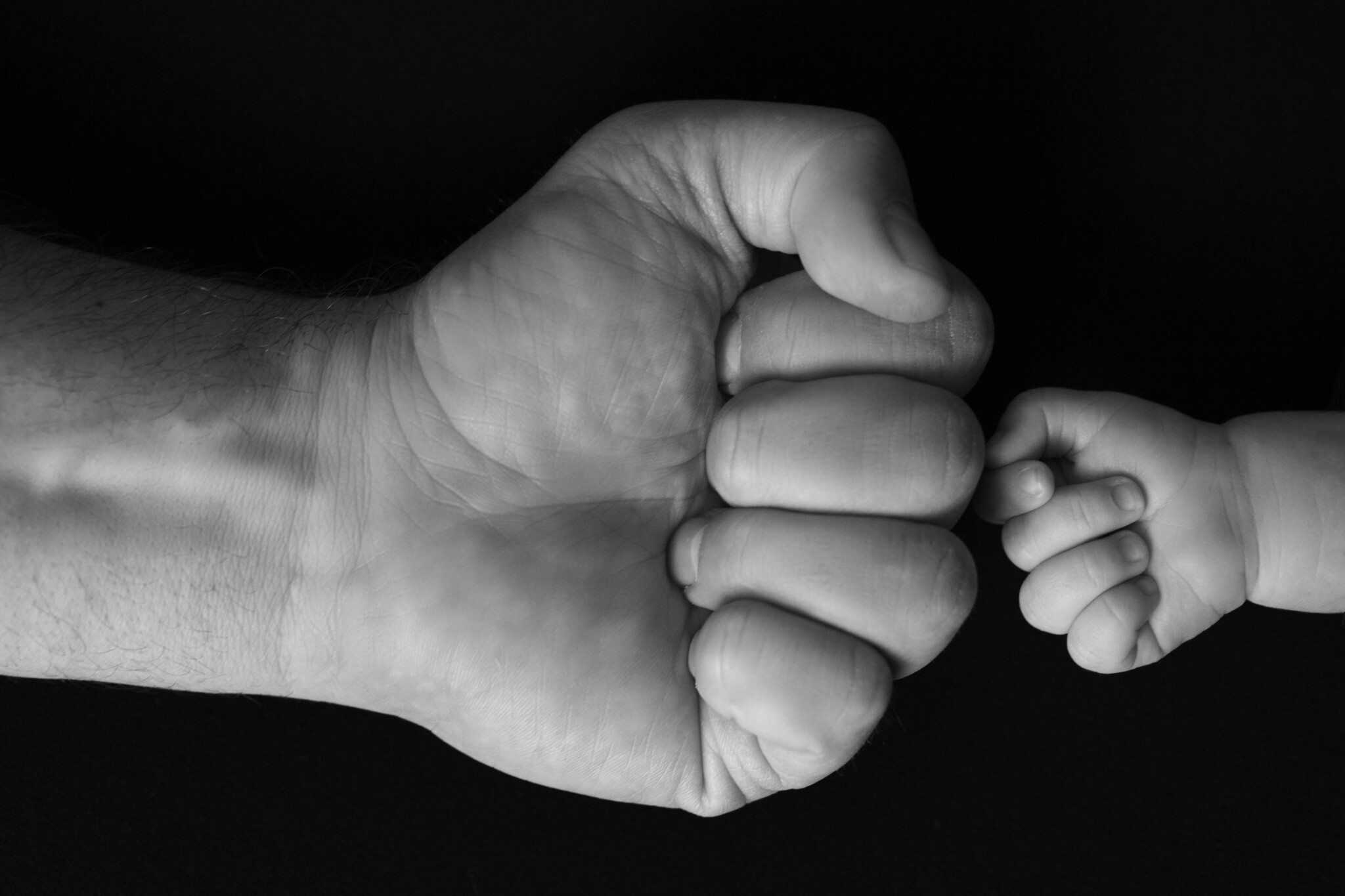 Tiny cute newborn fist in front of daddy's big fist