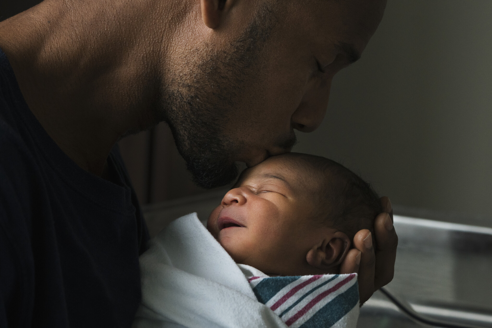 Black father kissing forehead of newborn son