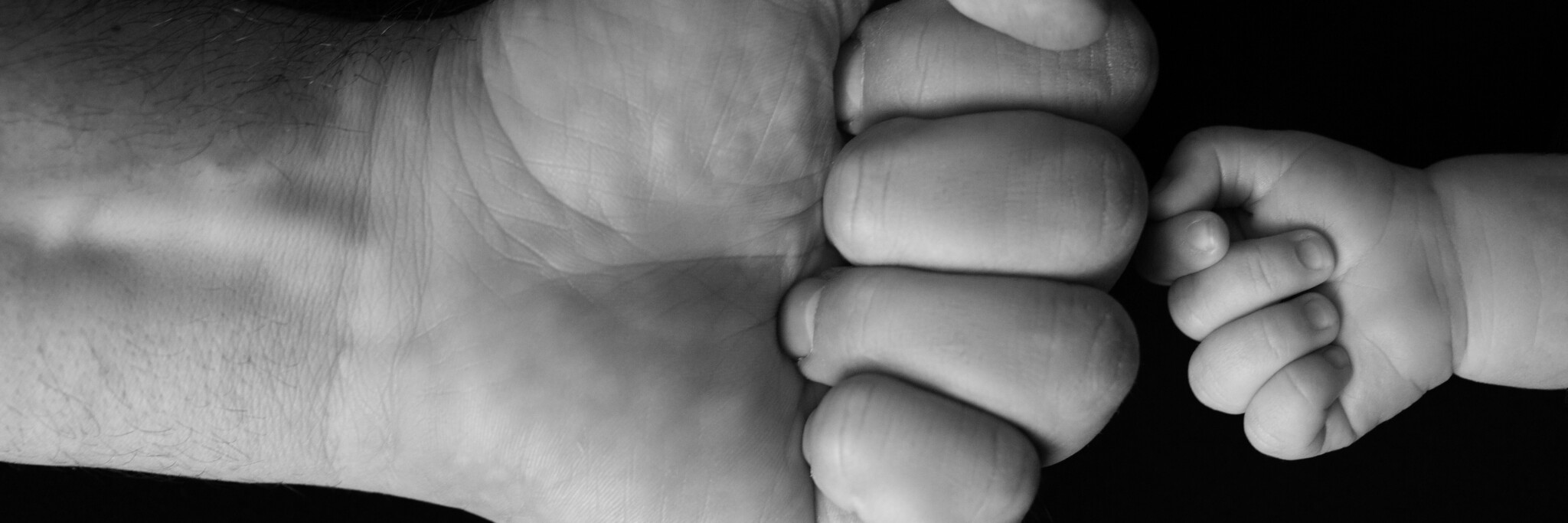 Newborn's fist in front of dad's fist on black background