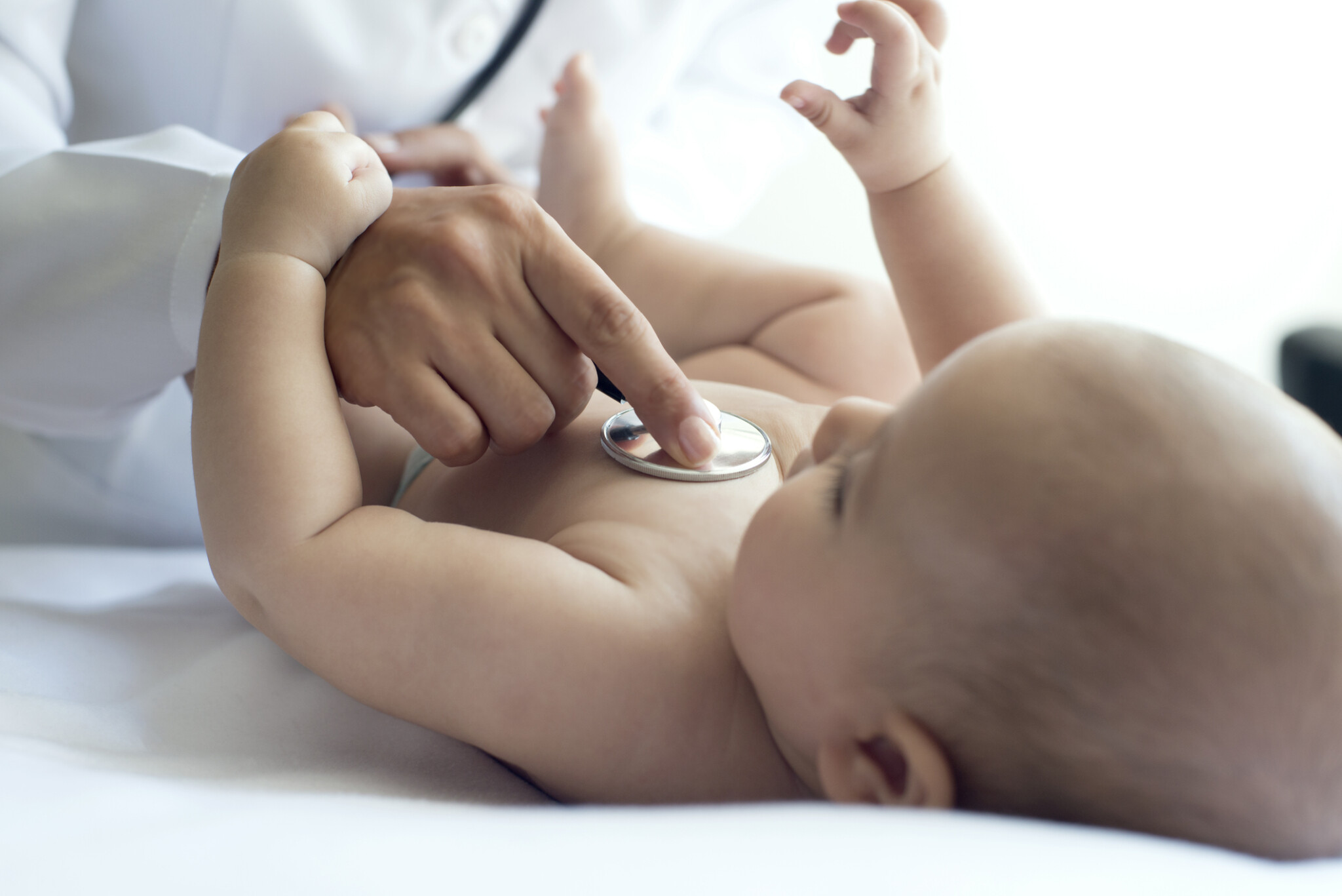 Baby laying on back plays with hand of pediatrician