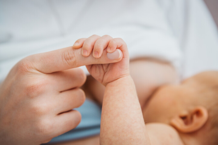 Close up of a baby holding mothers hand while breastfeeding.