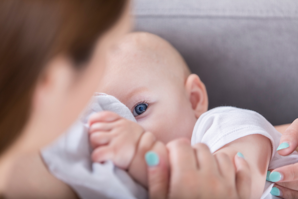 Blue eyed baby looks at mom while breastfeeding